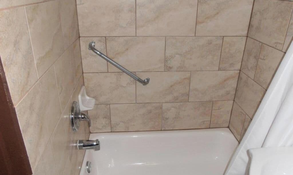 Un baño con bañera, barra de apoyo y toalla blanca.