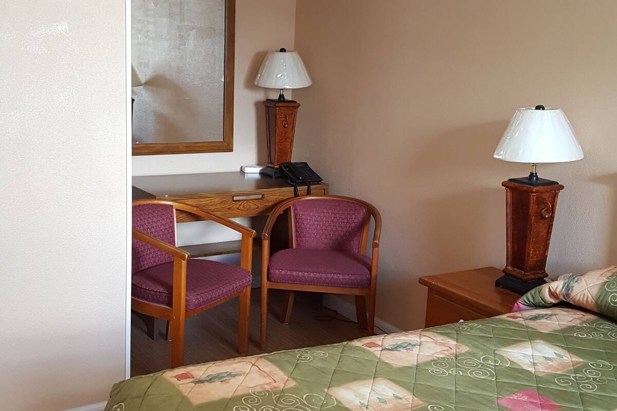 A hotel room with a bed, a desk, two chairs, two lamps, and a mirror on the wall.