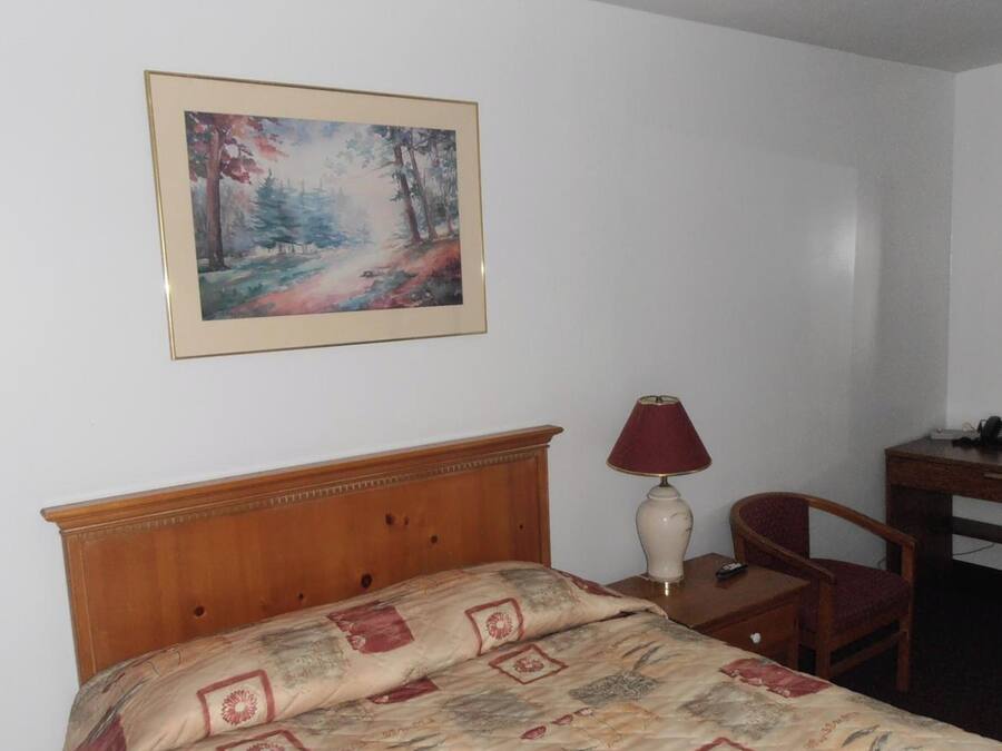 Une chambre d’hôtel avec un lit, un bureau doté d’une lampe, une chaise et un tableau accroché au mur.