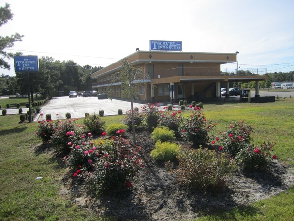 A Travel Inn & Suites building with a parking lot and flower beds in the foreground. - Travel Inn & Suites (Lakehurst)