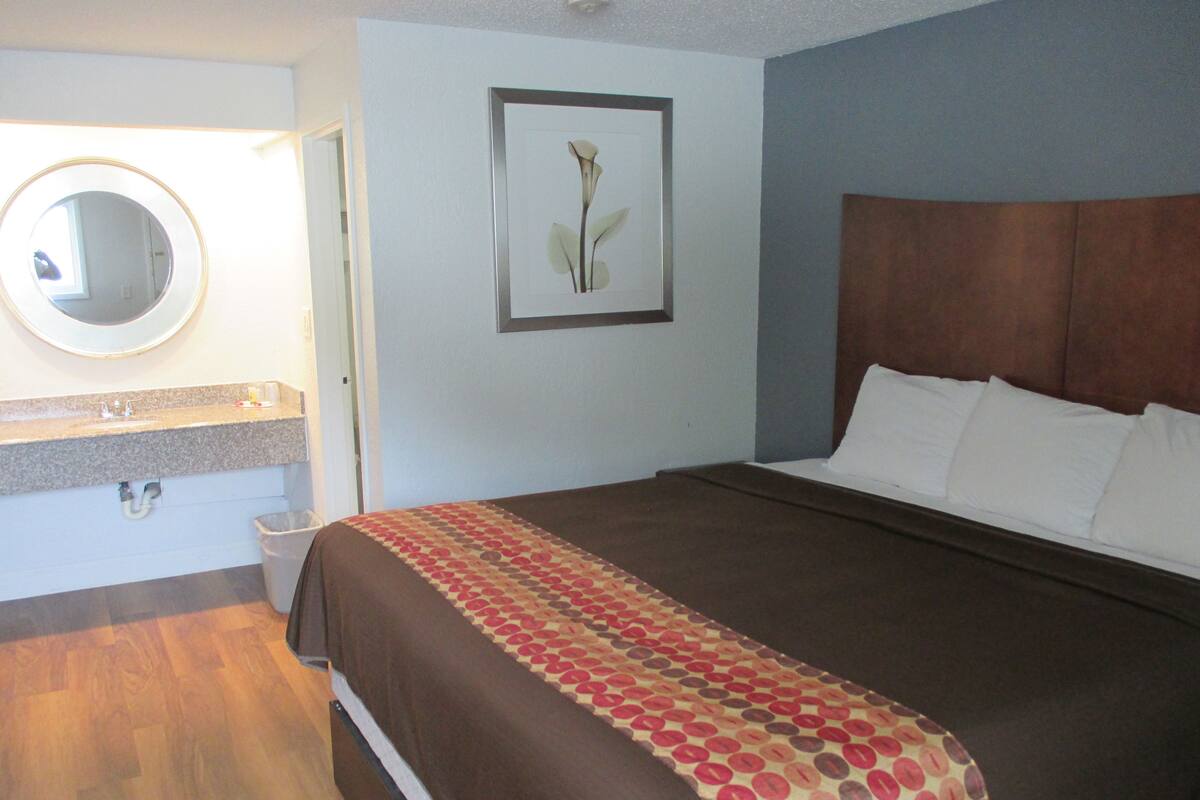 A hotel room with a bed, a bathroom with a sink and mirror, and a framed picture on the wall.