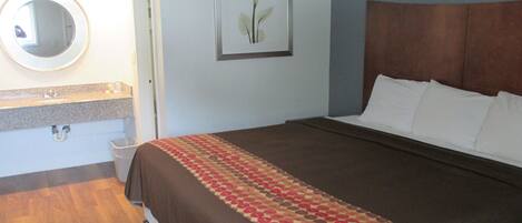 A hotel room with a bed, a bathroom with a sink and mirror, and a framed picture on the wall.