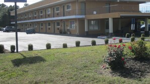 Edifício do Travel Inn & Suites com estrutura simples de dois andares, estacionamento e um pequeno jardim com flores vermelhas.