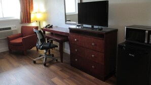 Quarto de hotel com escrivaninha de madeira, uma cadeira, televisão, cômoda e micro-ondas.