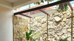 A stone wall, a bathtub, a chair, and potted plants in a room.