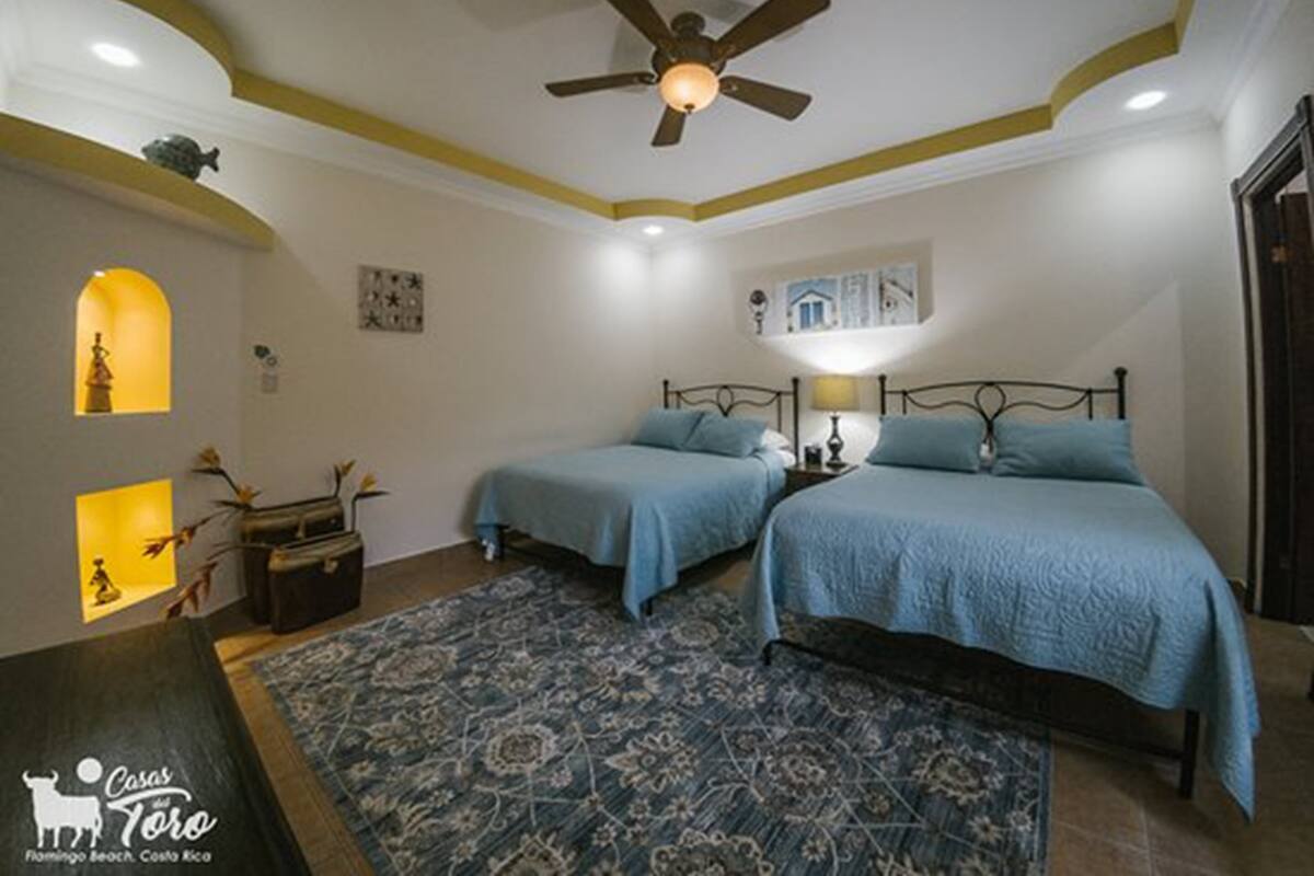 Ein Schlafzimmer mit zwei Betten, einem Deckenventilator und einem gemusterten Teppich.
