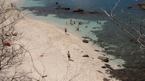Une plage avec une eau claire, des rochers et des gens qui se baignent.