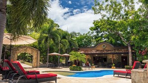 Un espace aménagé au bord de la piscine, avec des chaises longues, une piscine et un bâtiment doté d’un toit en tuiles.
