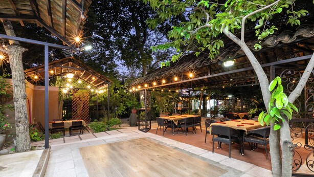 Un espace extérieur aménagé en terrasse, avec des tables et des chaises, des guirlandes lumineuses et une structure en forme de pergola.