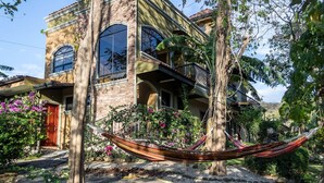 Une maison à deux étages dotée d’un balcon, entourée d’une végétation luxuriante et agrémentée d’un hamac.