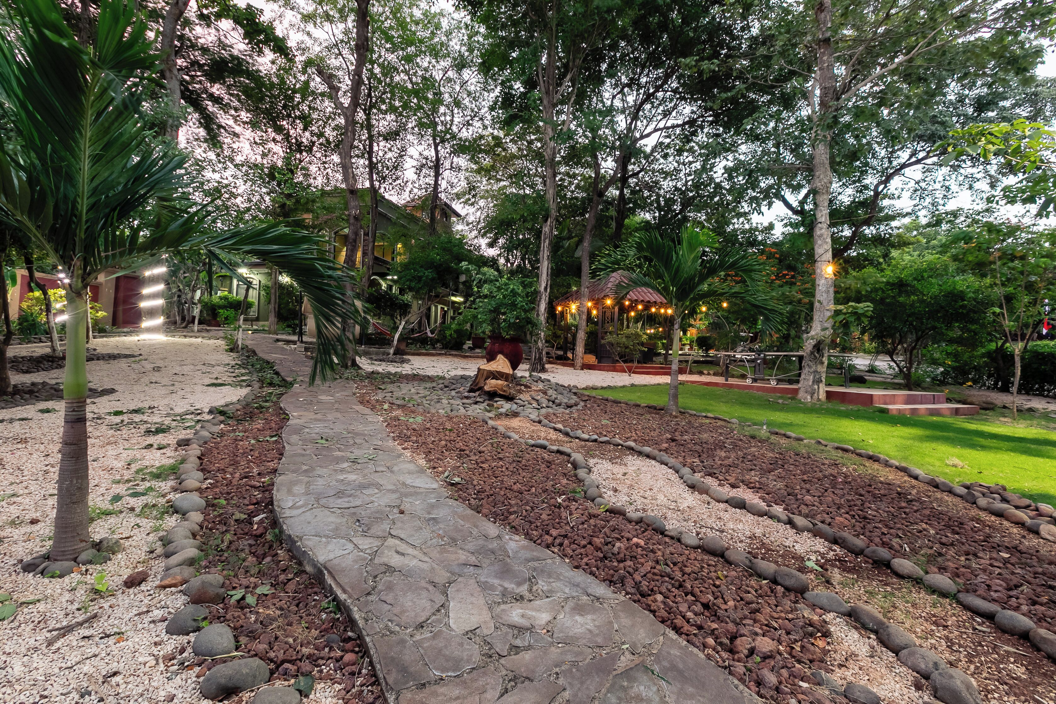 Un sentiero nel giardino, delimitato da pietre, circondato da alberi e un gazebo.