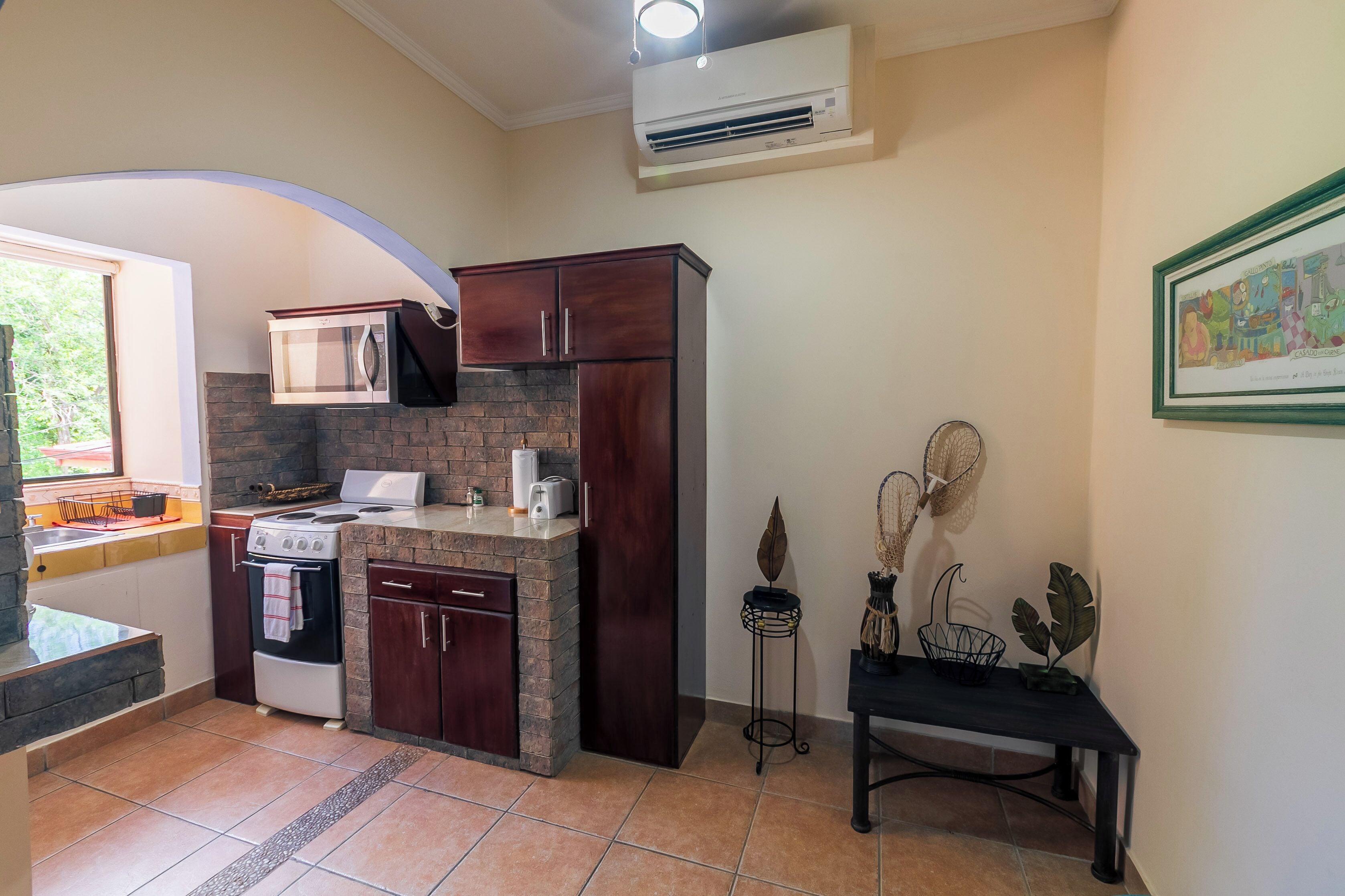 A compact kitchen with a built-in stove, microwave, and oven, a small dining area with a bench, and a decorative plant.
