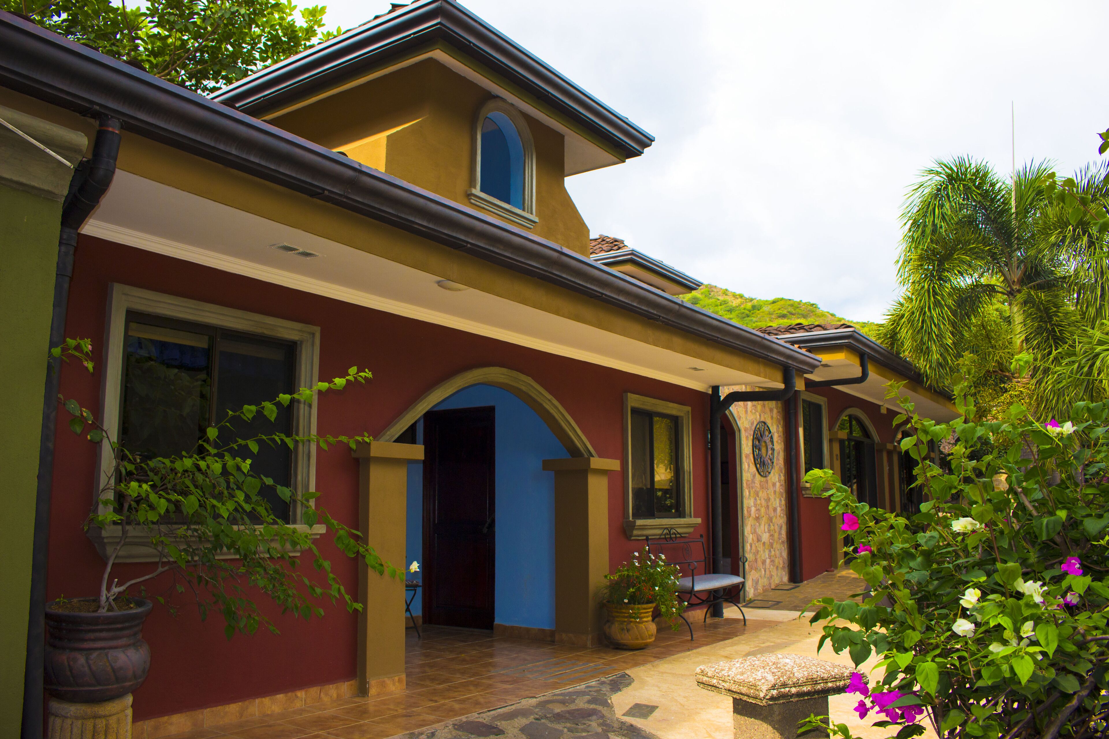 Una casa a due piani con una facciata rossa, una porta blu e un piccolo portico con una panchina.