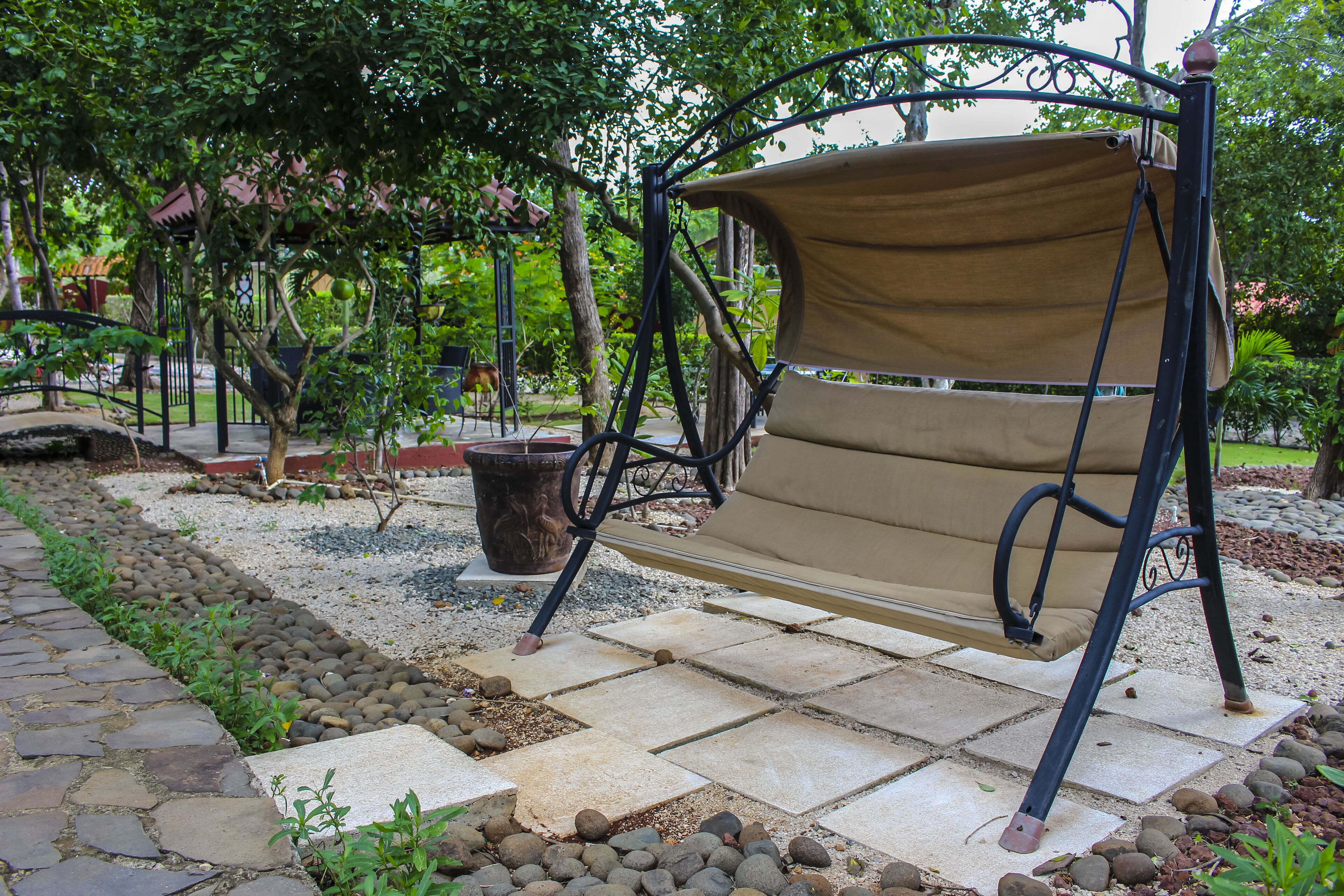 Un jardín con un columpio, un sendero de piedra y una cerca de metal.