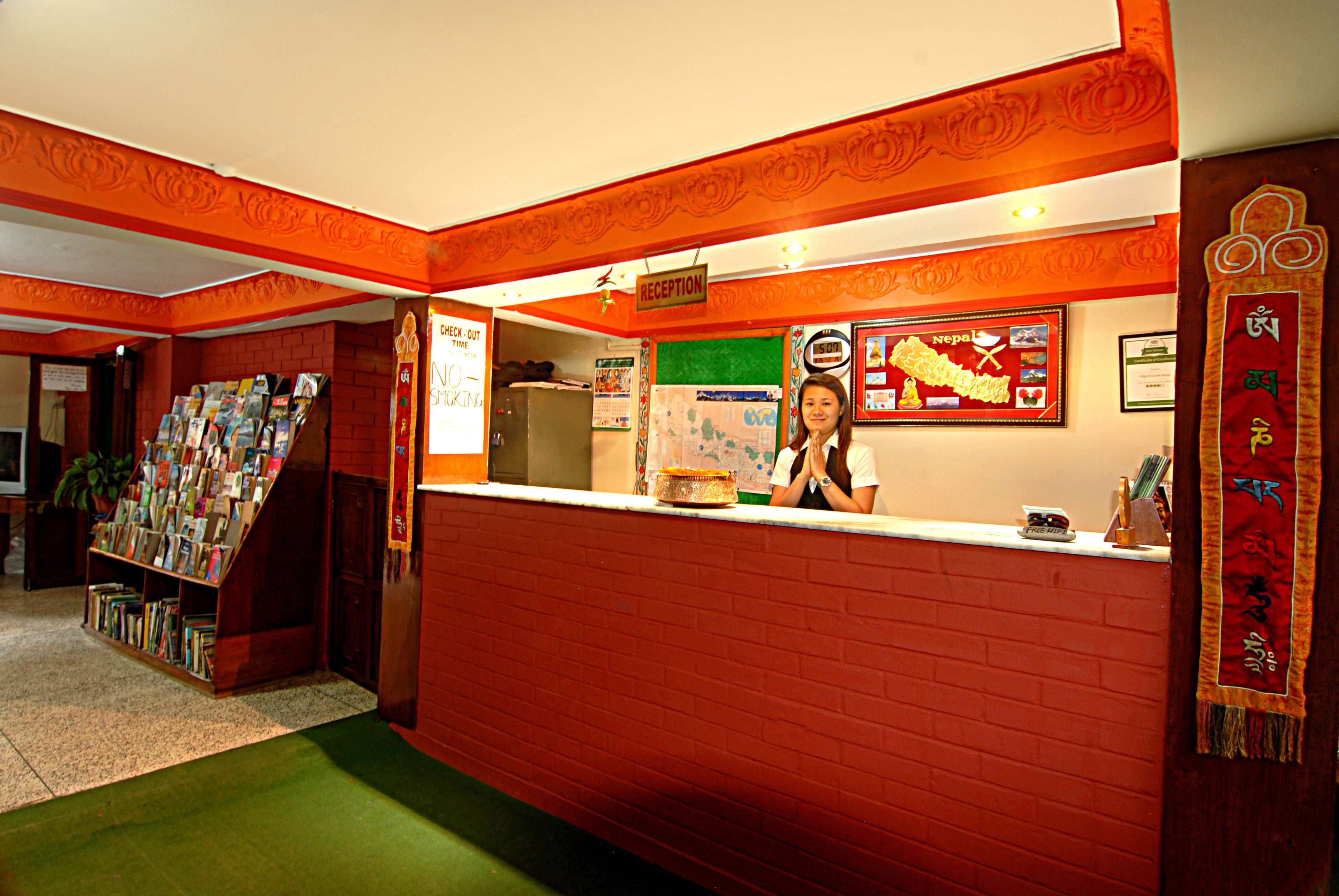 A reception area with a red brick wall, a reception desk, a framed welcome sign, and a bookshelf filled with magazines.