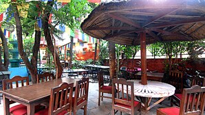 An outdoor dining area with wooden tables and chairs, a thatched umbrella, and colorful flags. - Pilgrims Guest House (Kathmandu)