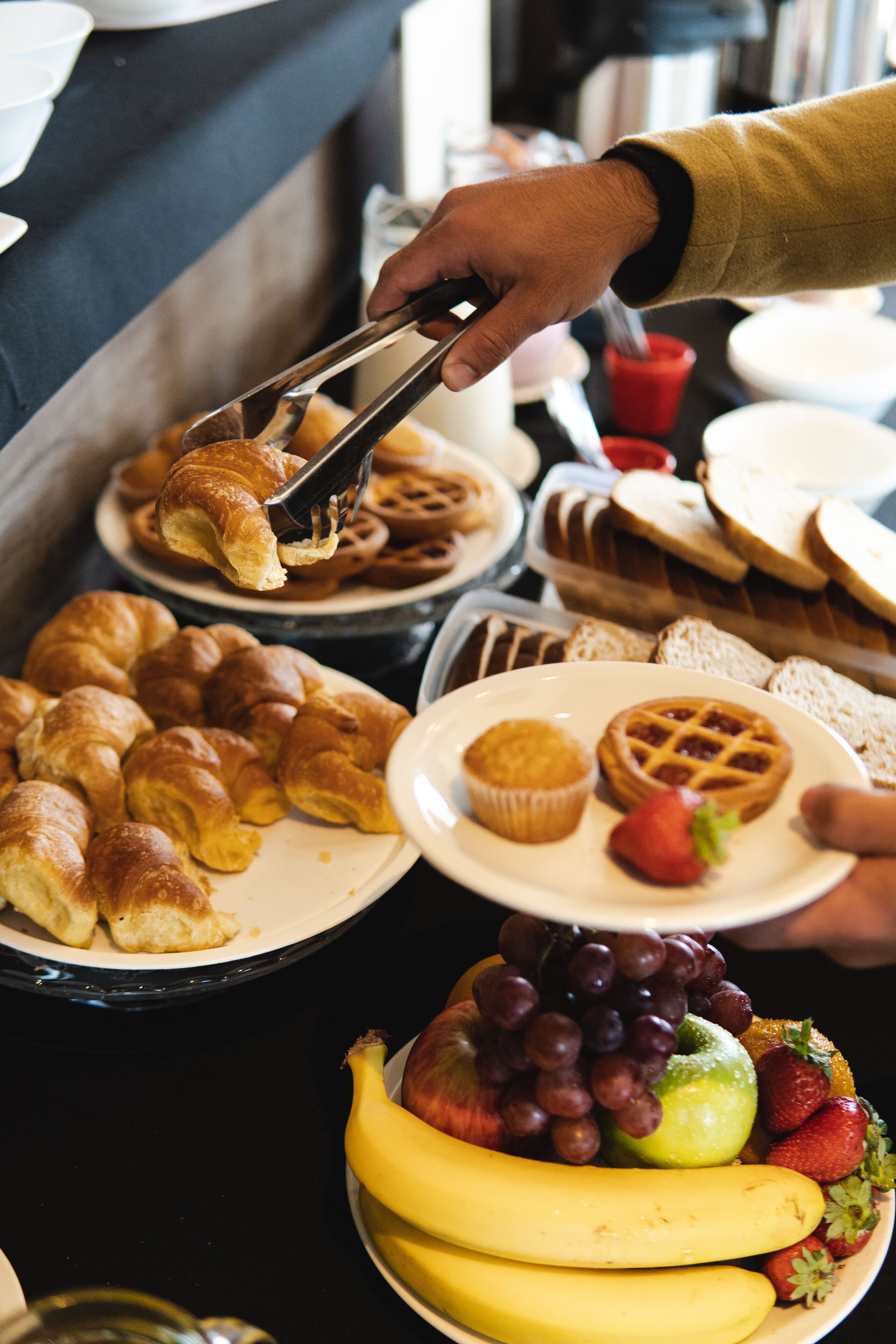 A buffet with various food items including croissants, waffles, and fruits.