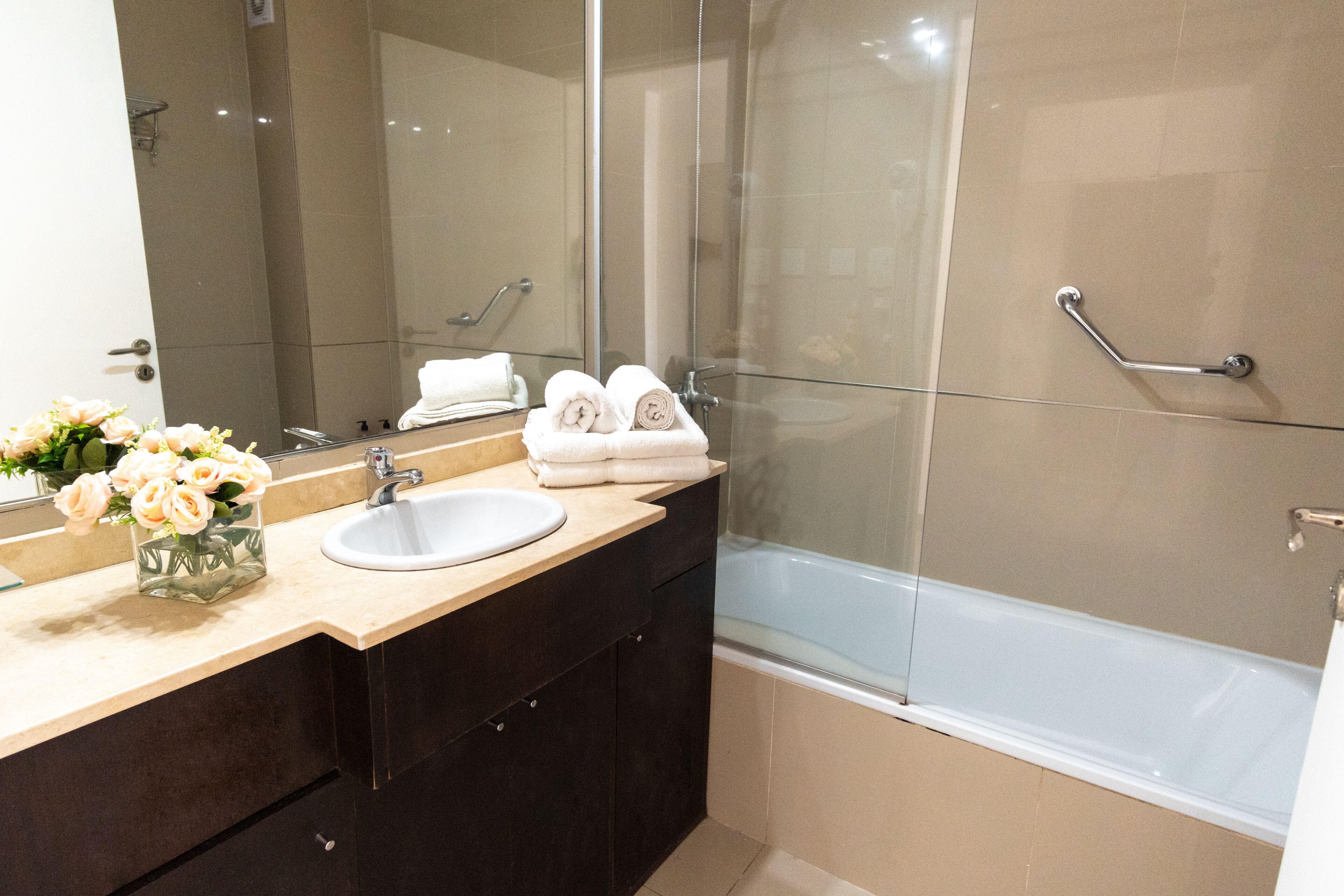 Un bagno moderno con box doccia in vetro, lavandino bianco e mobile contenitore con ante scure.
