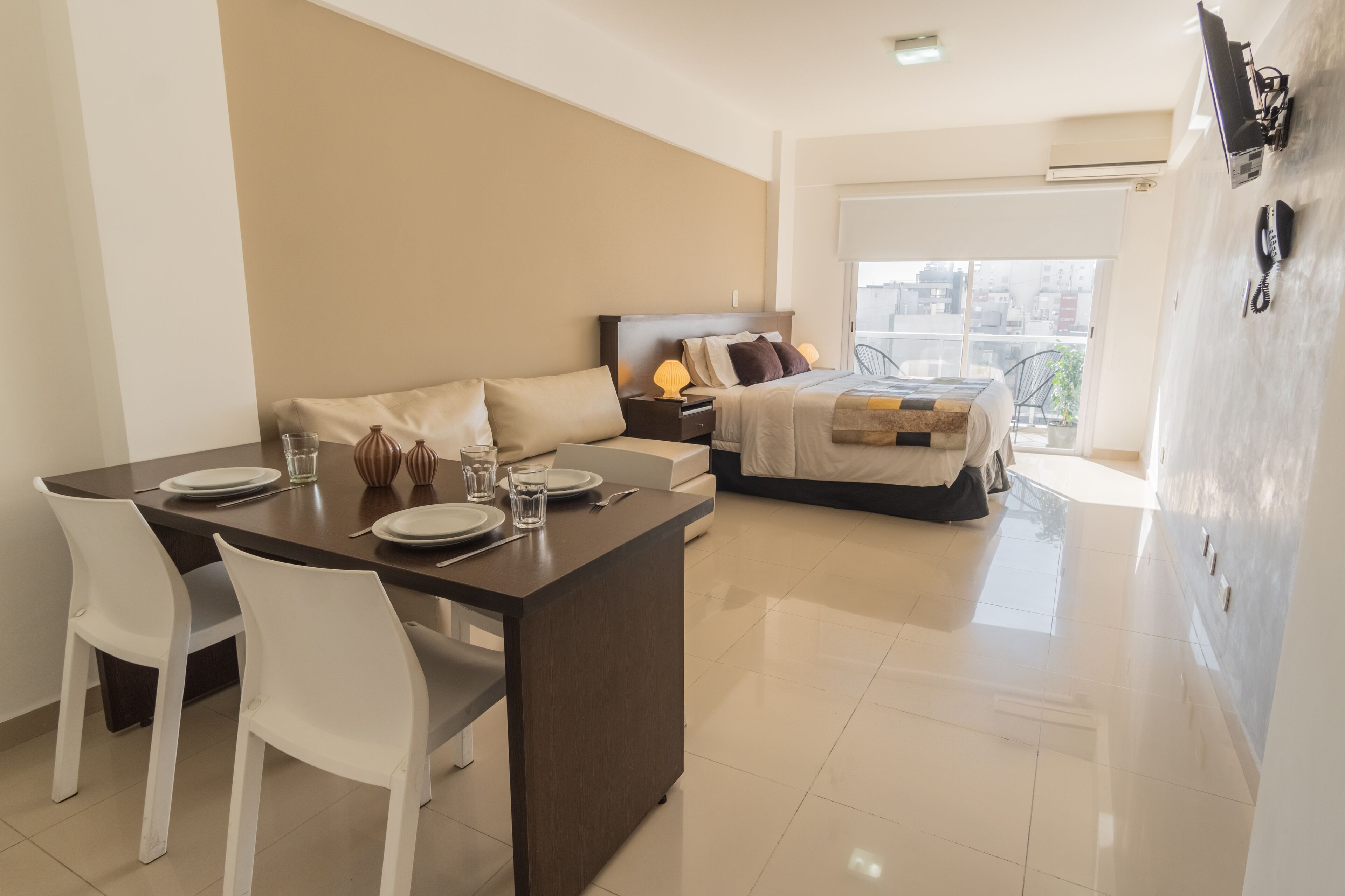 A modern hotel room with a dining area, a bed with a view, and a balcony.