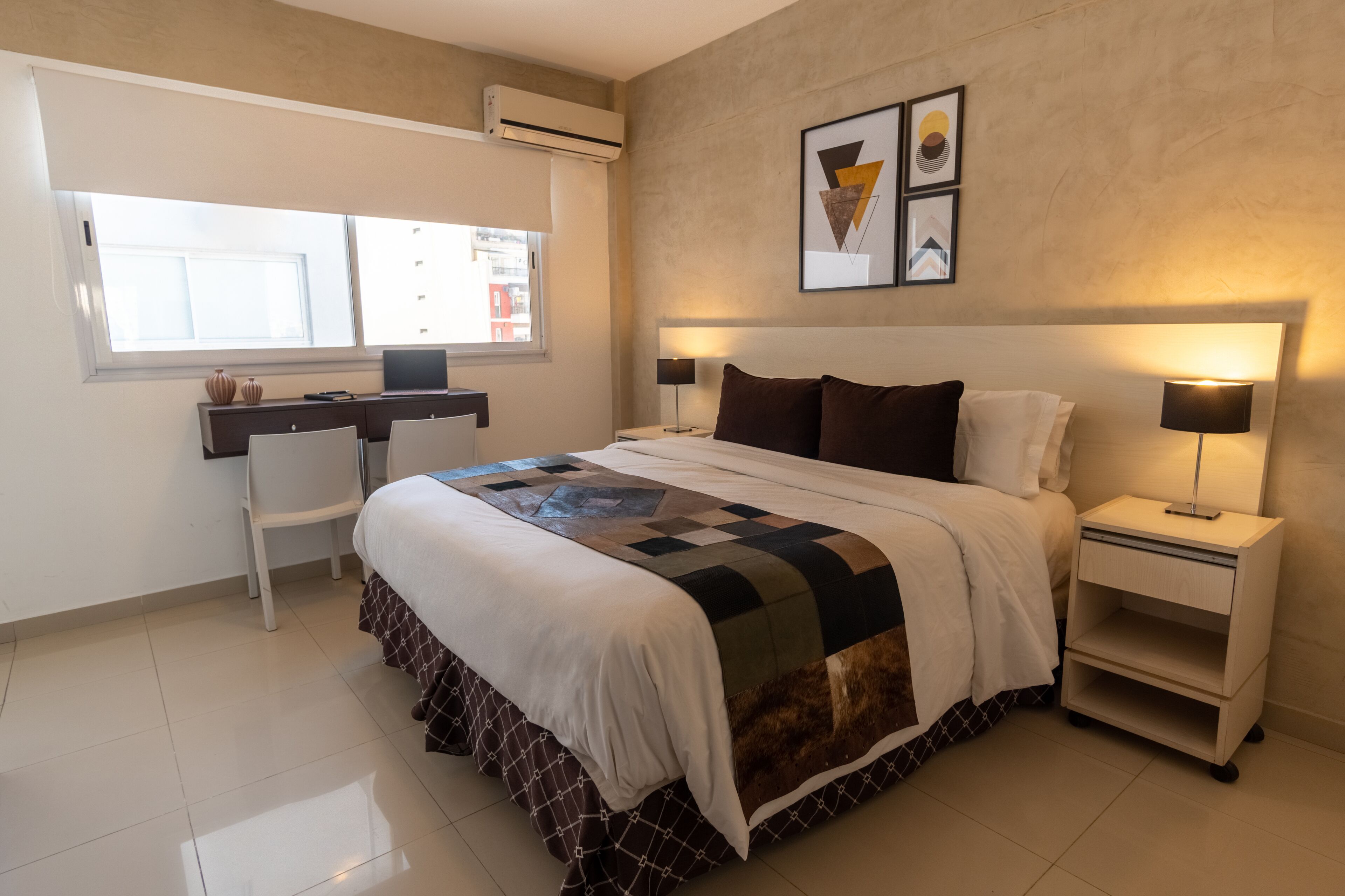 A neatly arranged bedroom with a bed, bedside tables, a desk, and a chair.
