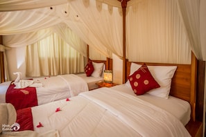 A room with two beds, each with white linens and red pillows, a wooden headboard, and a nightstand with a lamp. - Rama Shinta Hotel (Karangasem)