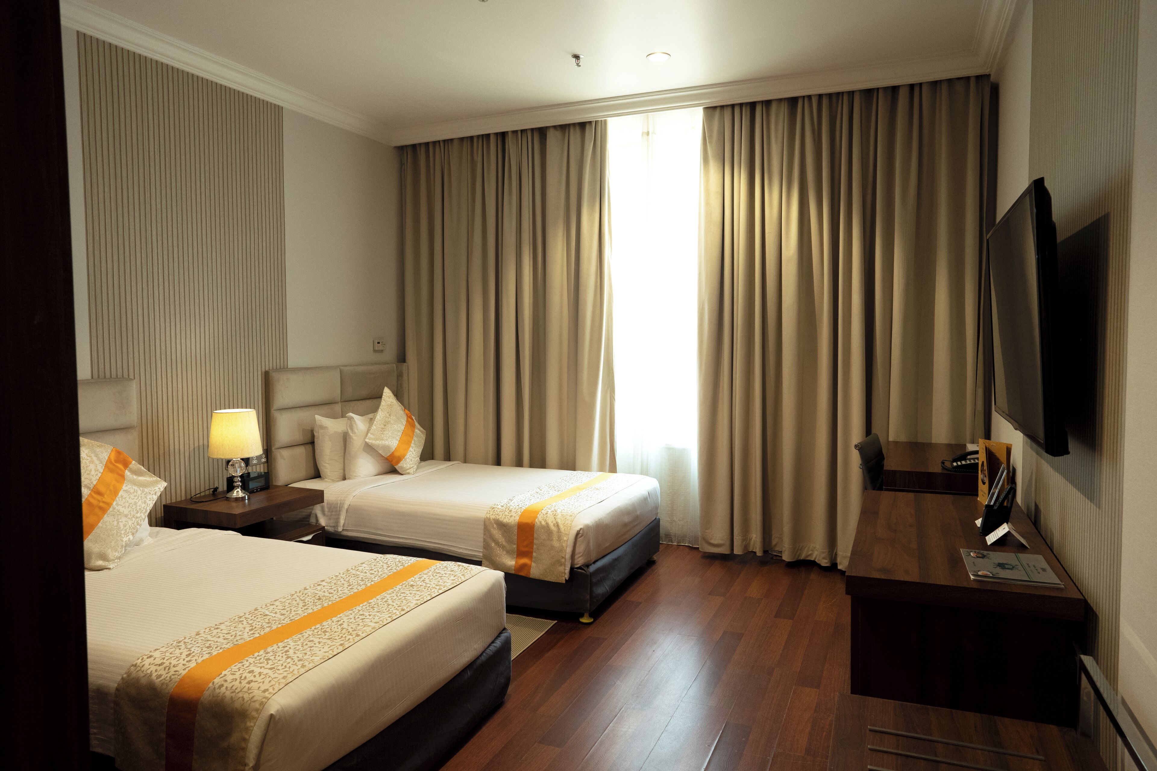 Habitación de hotel con dos camas, un escritorio, un televisor y una ventana con cortinas.