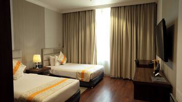 Habitación de hotel con dos camas, un escritorio, un televisor y una ventana con cortinas.