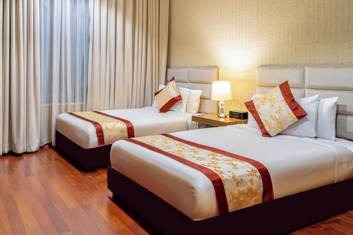 Une chambre d’hôtel avec deux lits, une table de chevet avec une lampe et une fenêtre avec des rideaux.