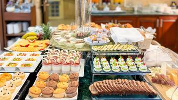 Un bufé con diversas opciones de comida, incluyendo pasteles, postres y frutas.