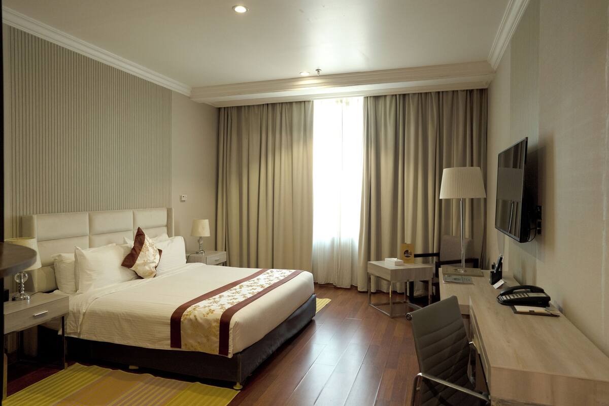 Une chambre d’hôtel avec un grand lit, un bureau, une chaise, une télévision et une fenêtre avec des rideaux.