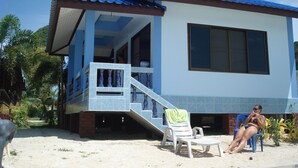 A two-story building with a blue roof and white walls, featuring a covered outdoor seating area with a chair and a table.