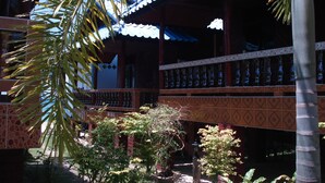 A traditional building with a tiled balcony, surrounded by greenery and a clear blue sky.