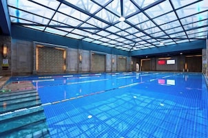 Una piscina interior con techo de vidrio, paredes de azulejos y una vista despejada del cielo.