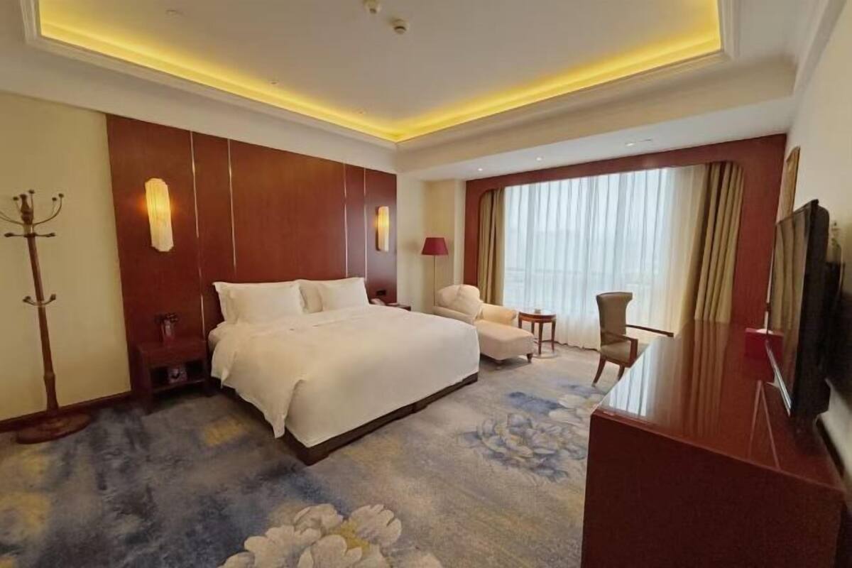 Une chambre d’hôtel avec un grand lit, un coin salon comprenant une chaise et une petite table, une télévision et un porte-manteau.