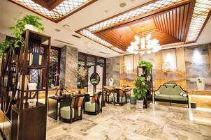 Un hall de hotel con mostrador de recepción, zona de estar y plantas decorativas.