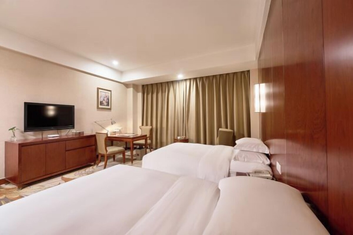 A hotel room with a large bed, a desk with a chair, a television, and a window with curtains.