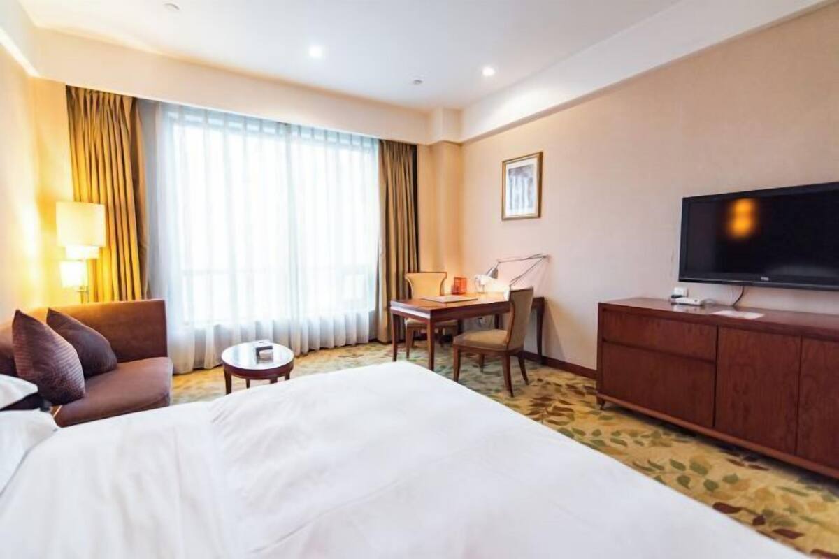 Une chambre d’hôtel avec un grand lit, un bureau, une chaise, une télévision et un canapé.