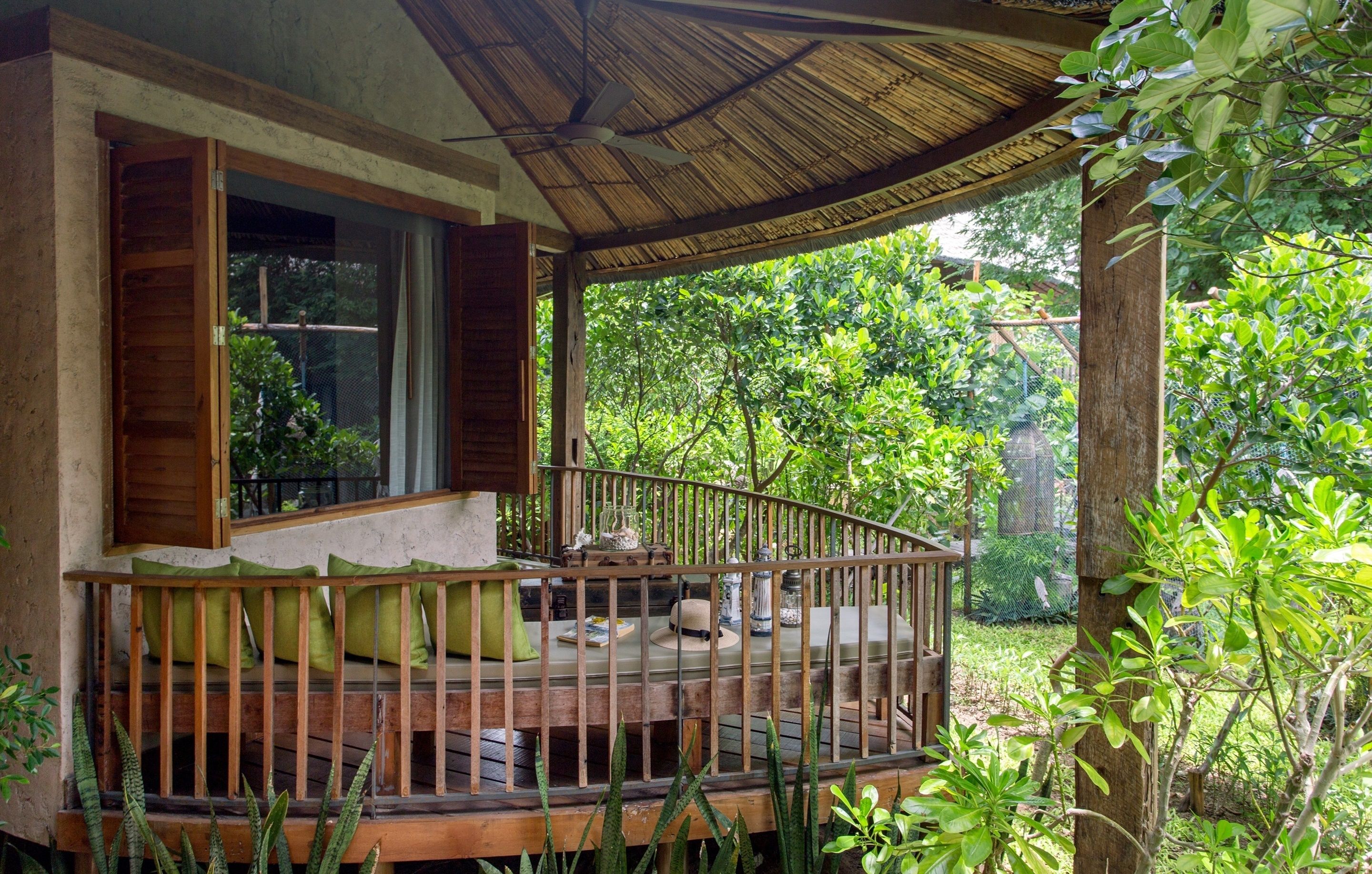 A wooden deck with a railing, a table with chairs, and a thatched roof structure.