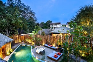 Un área de piscina con cubierta de madera, asientos de descanso y cerramiento de bambú.