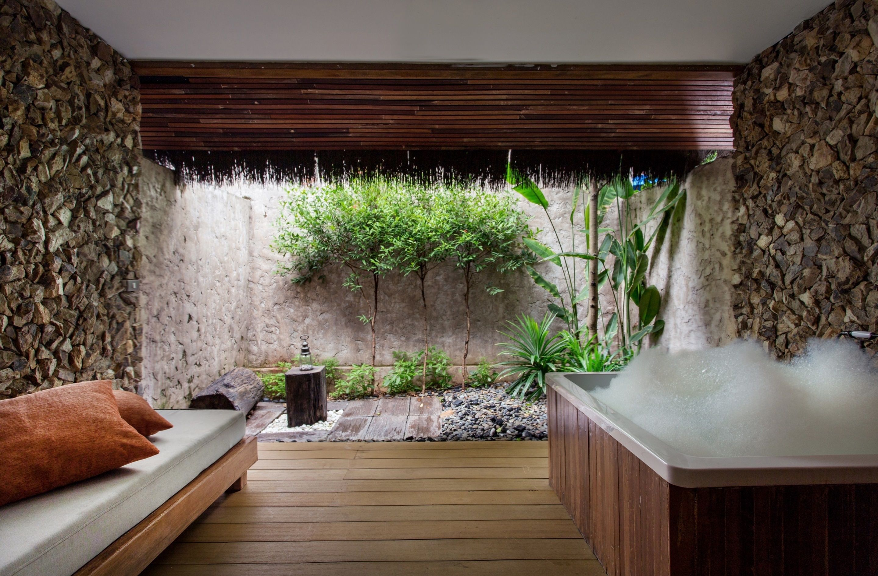 A spa area with a wooden deck, a hot tub, and a stone wall with greenery.