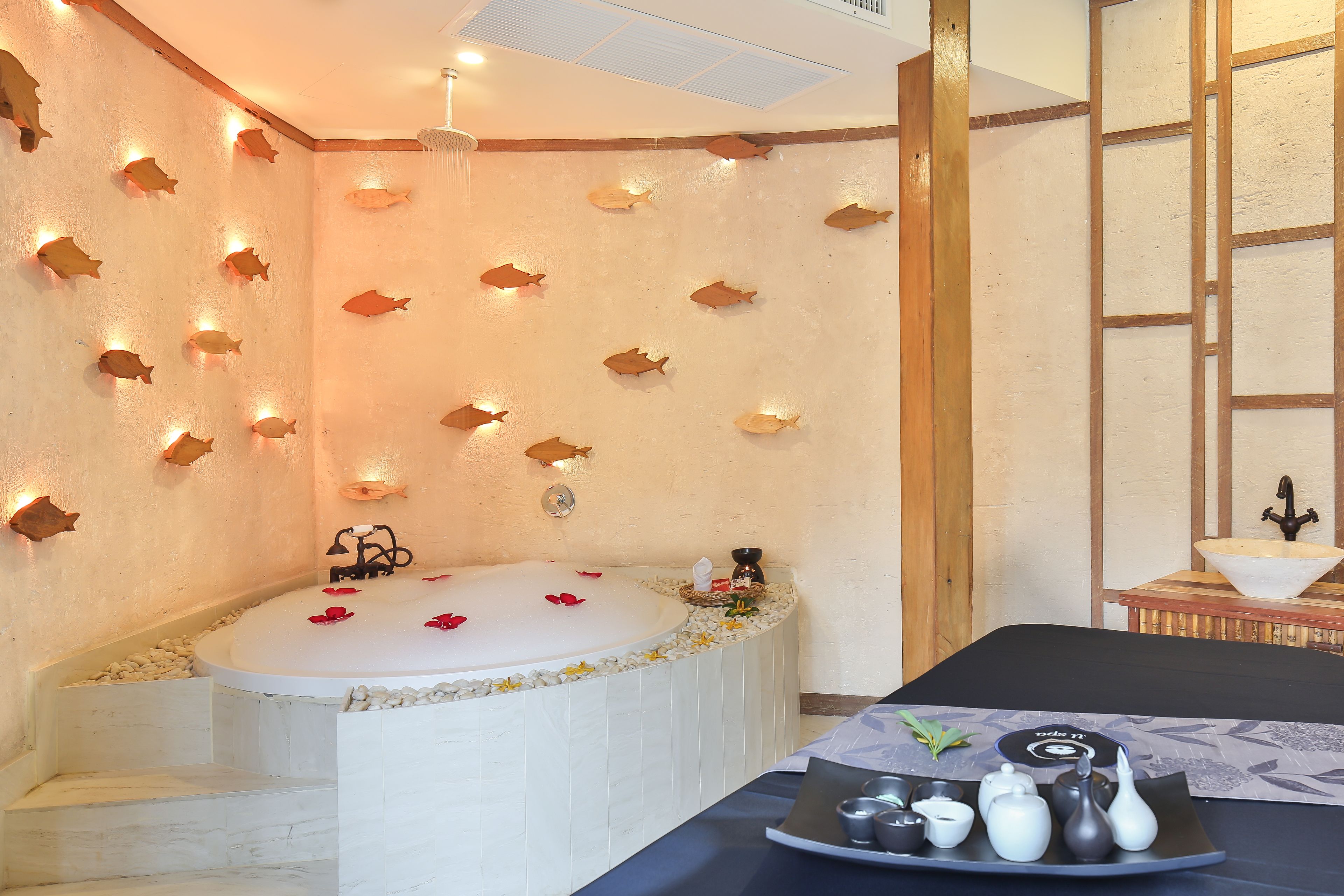 A spa room with a large bathtub, wooden wall decor, and a table with tea set.