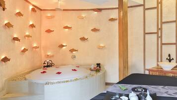 A spa room with a large bathtub, wooden wall decor, and a table with tea set.