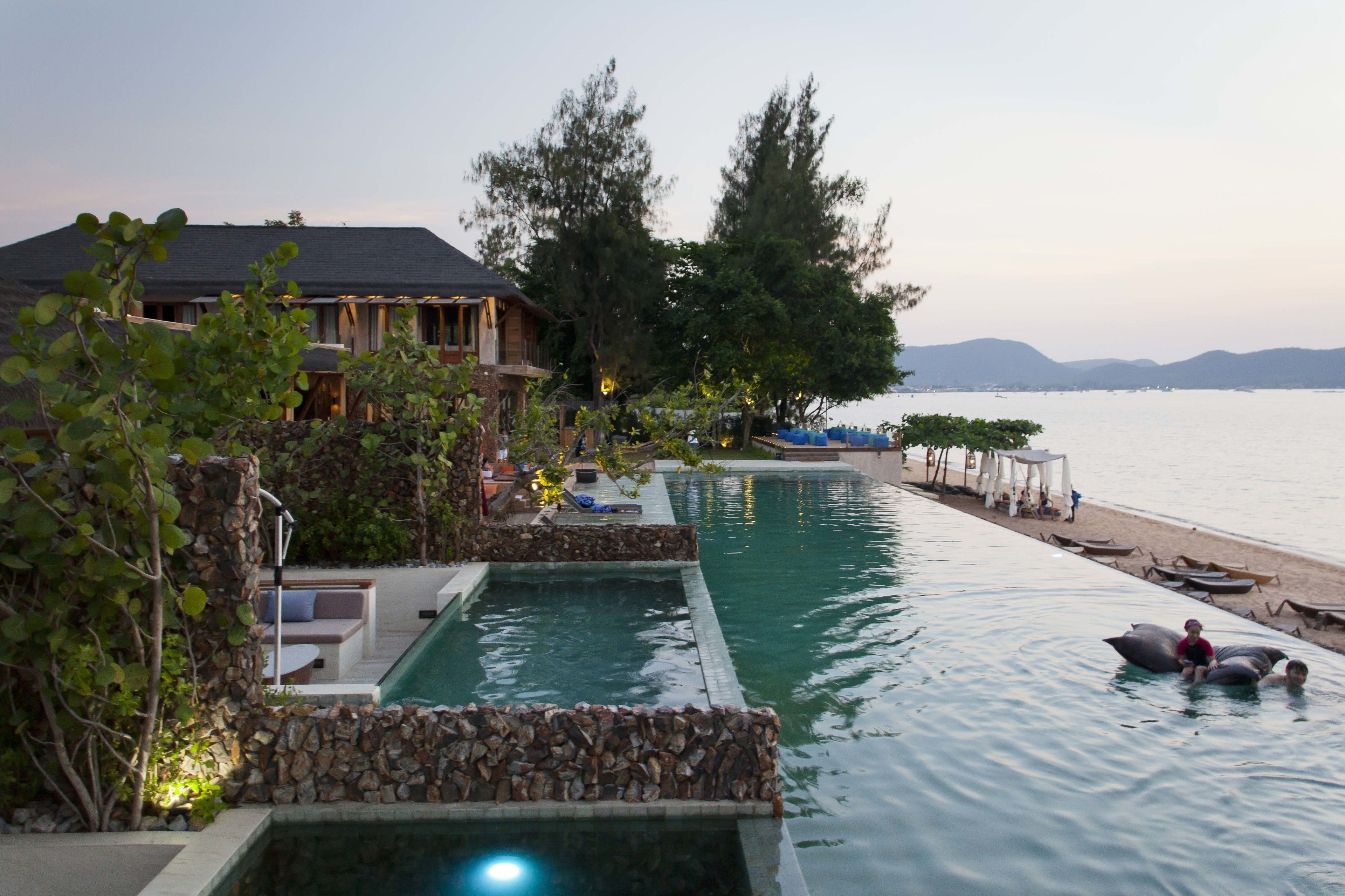 A resort with a swimming pool, a beach area, and a large tree.