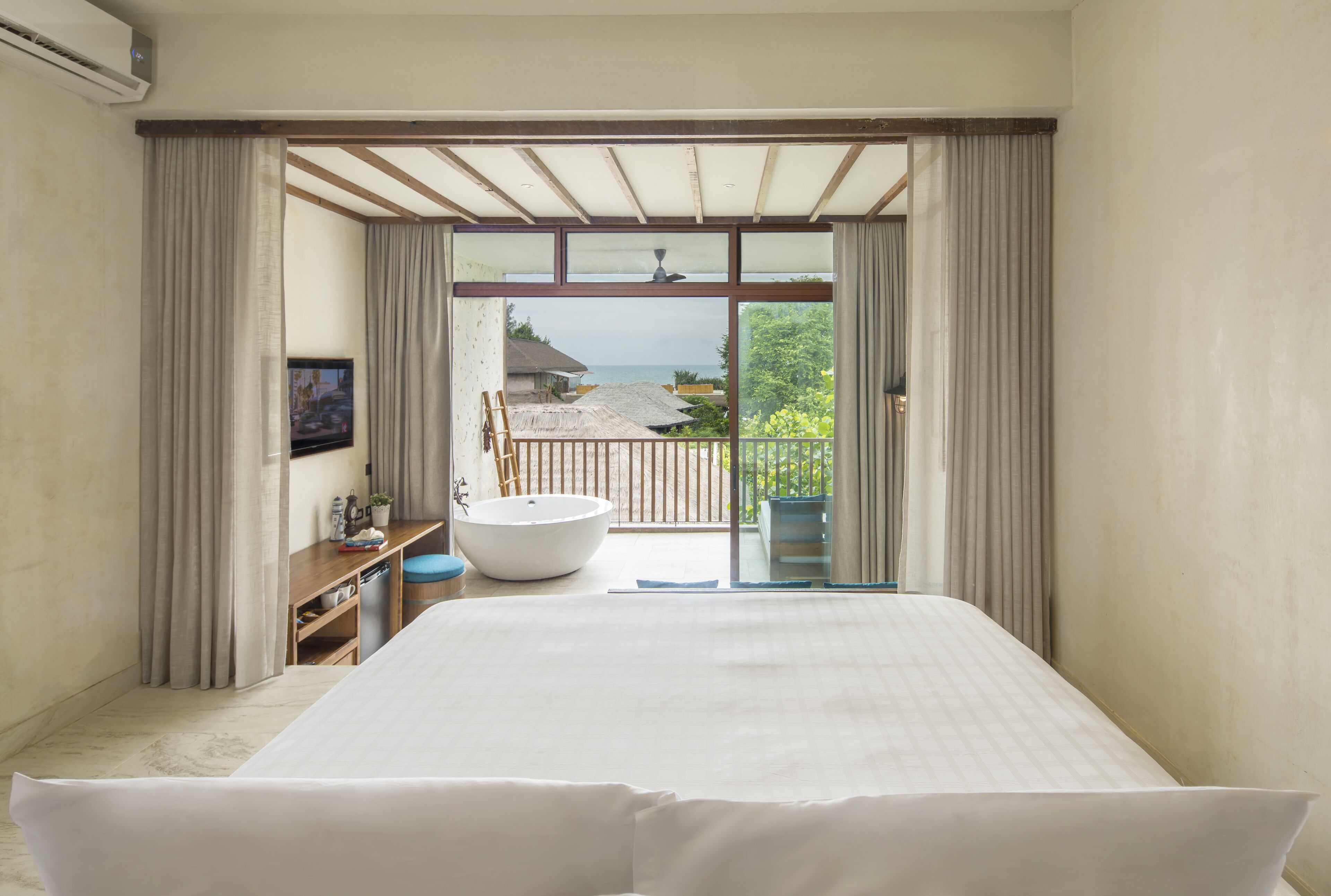 Un dormitorio amplio con una cama grande, una bañera integrada y un balcón con vistas al mar.