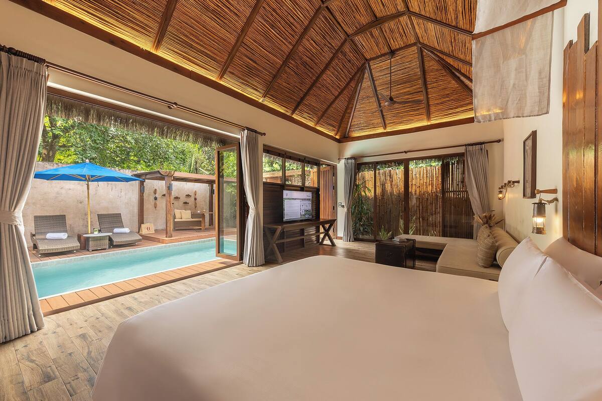 A spacious bedroom with a large bed, a television, and a view of an outdoor pool area.