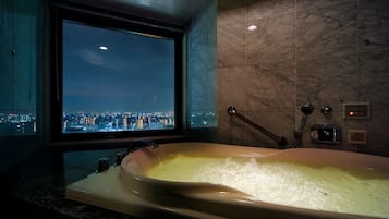 Un baño moderno con una bañera grande, vistas de la ciudad a través de una ventana y paredes de mármol.