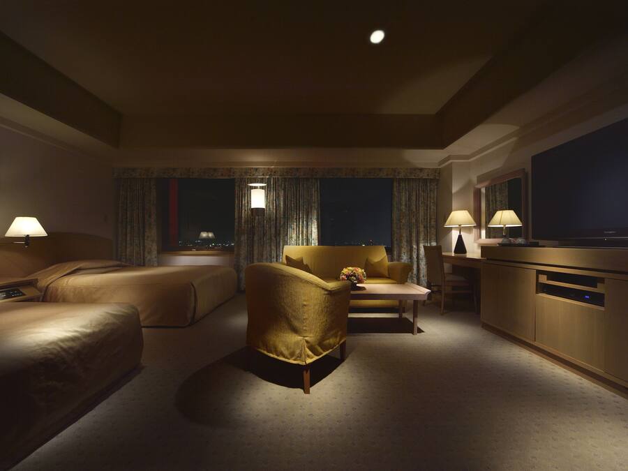 A hotel room with a sofa, armchair, and a TV.