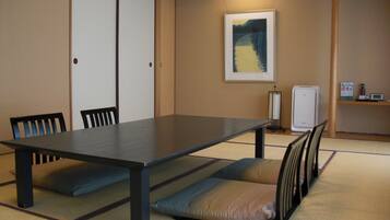 A conference room with a long table, chairs, tatami mats, a framed picture on the wall, and a small refrigerator.