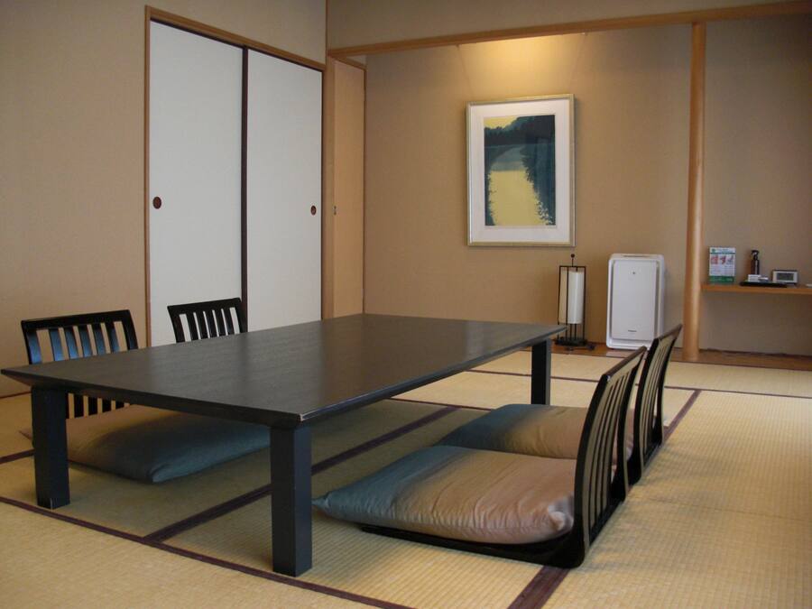 A conference room with a long table, chairs, tatami mats, a framed picture on the wall, and a small refrigerator.