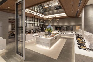 A modern hotel lobby with a central island, seating area, and a kitchen in the background. - Royal Pines Hotel Urawa (Saitama)
